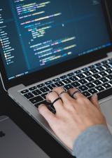 Hands typing on a keyboard. The screen displays coding language.